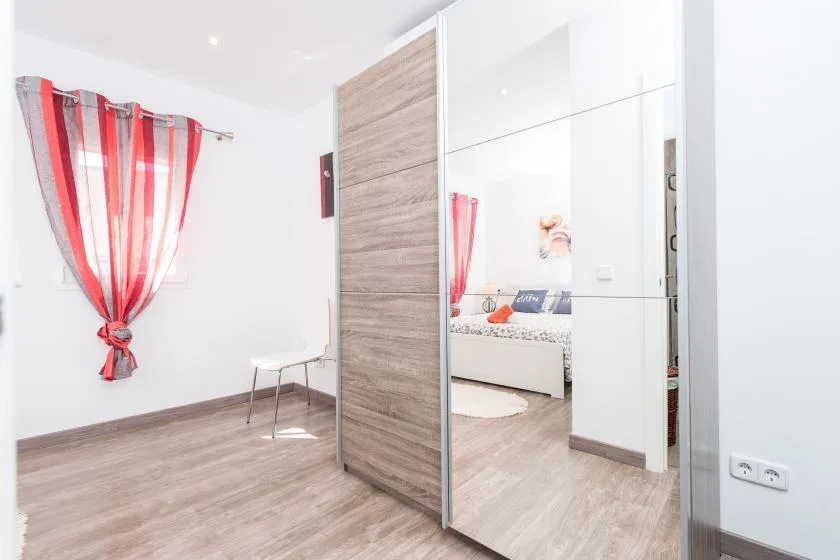 A bright bedroom with a mirrored wardrobe and red-striped curtains.