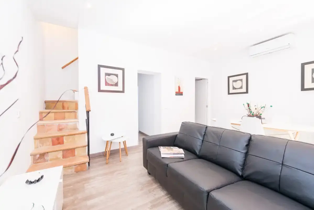 A bright living room with a dark sectional sofa and a staircase.