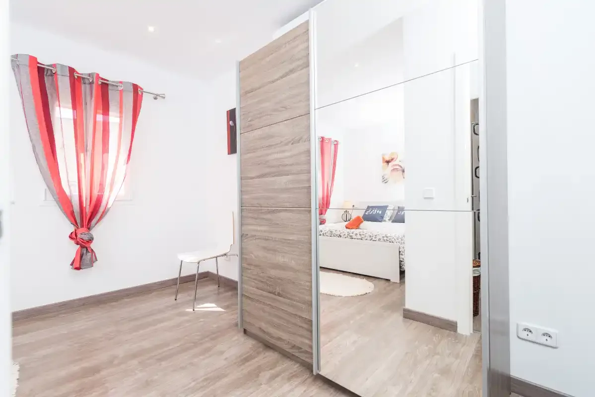 A bright bedroom with a red striped curtain and a mirrored wardrobe.
