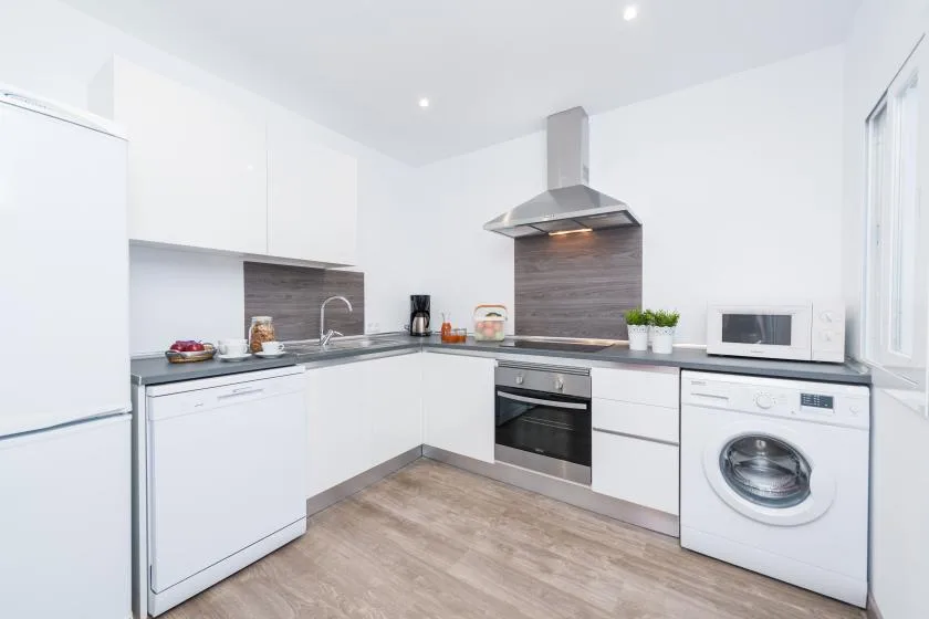 A bright white kitchen with an L-shaped counter, oven, and washing machine.