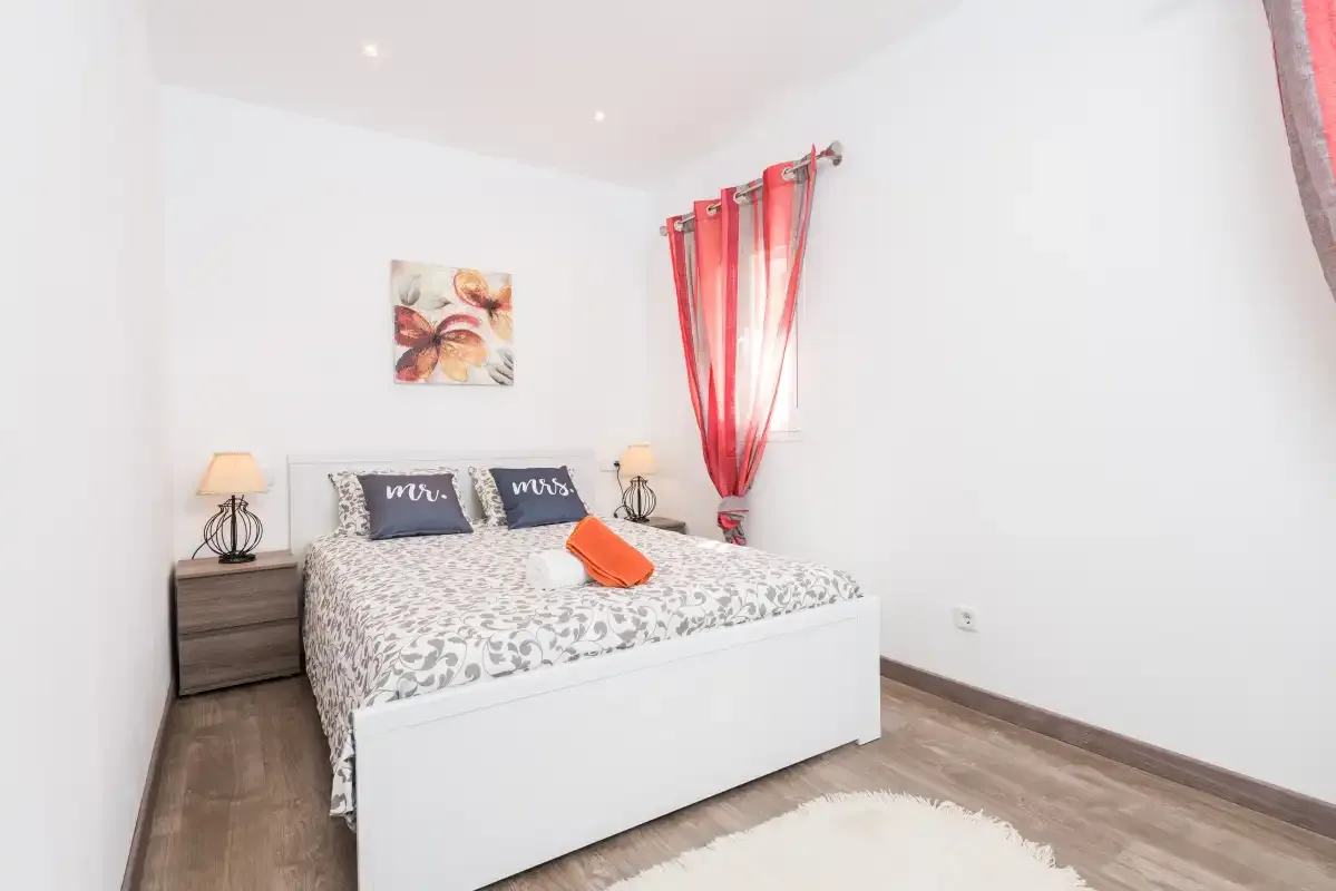 A bedroom with a double bed, bedside tables, and red curtains.