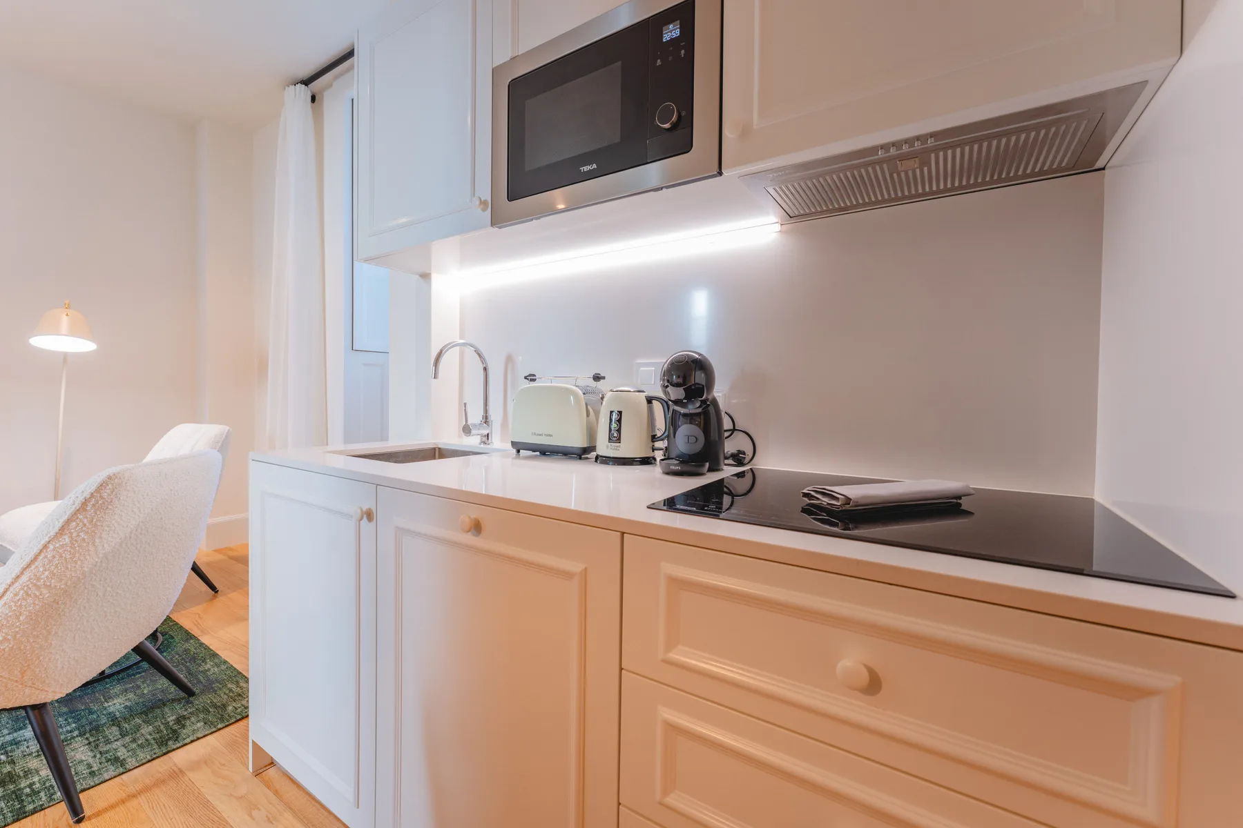 Una cocina compacta con gabinetes blancos, una placa de cocción y pequeños electrodomésticos.