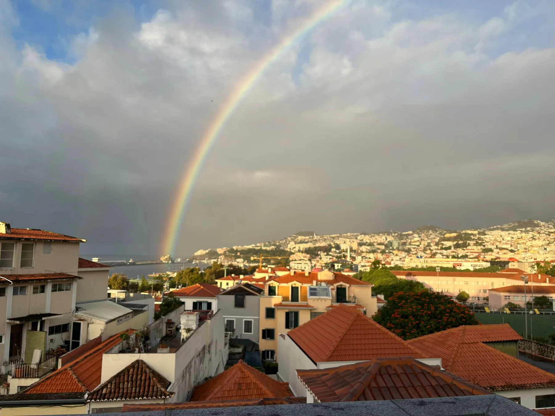 Un arcoíris se extiende sobre un barrio en la ladera, con edificios y tejados.