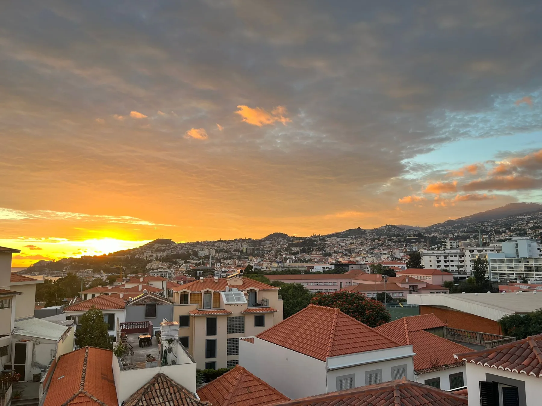 Un paisaje urbano de edificios con tejados rojos bajo un cielo colorido al atardecer.