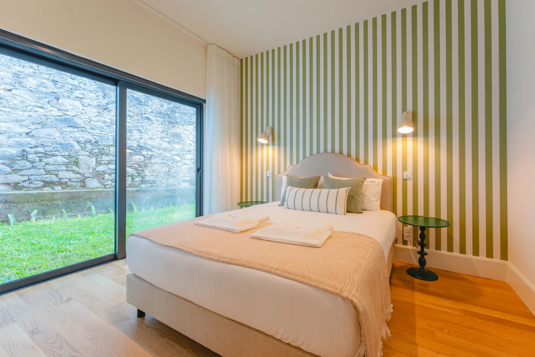 Un dormitorio con una cama junto a una gran ventana con vistas a un jardín.