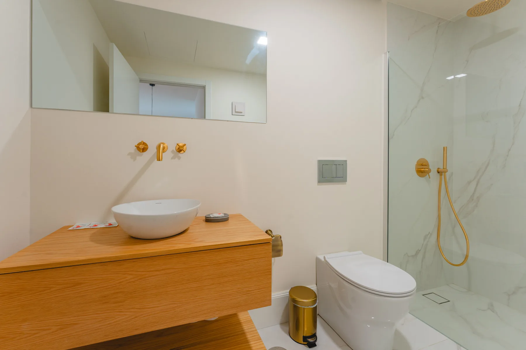 Un baño con mueble de madera, lavabo sobre encimera, inodoro y ducha de vidrio.