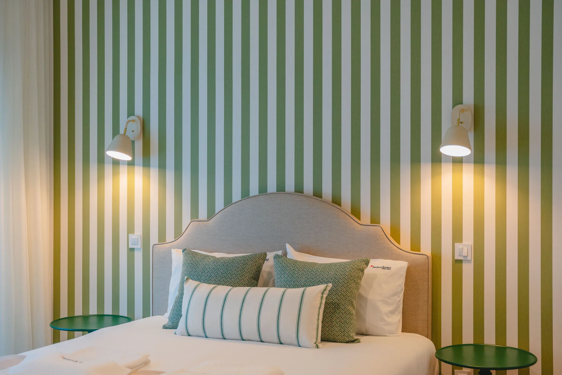 Un dormitorio con una cama junto a una pared de rayas verdes y blancas.