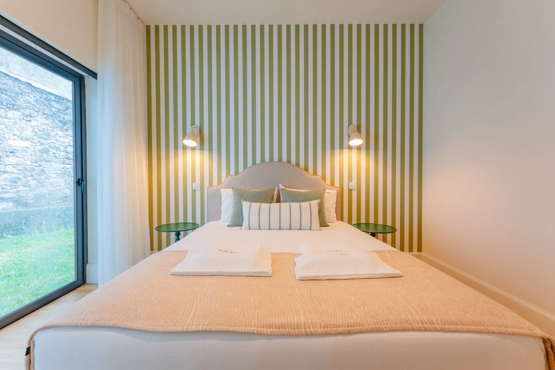 Un dormitorio con una cama frente a una pared de rayas verdes y blancas y una gran puerta de cristal.