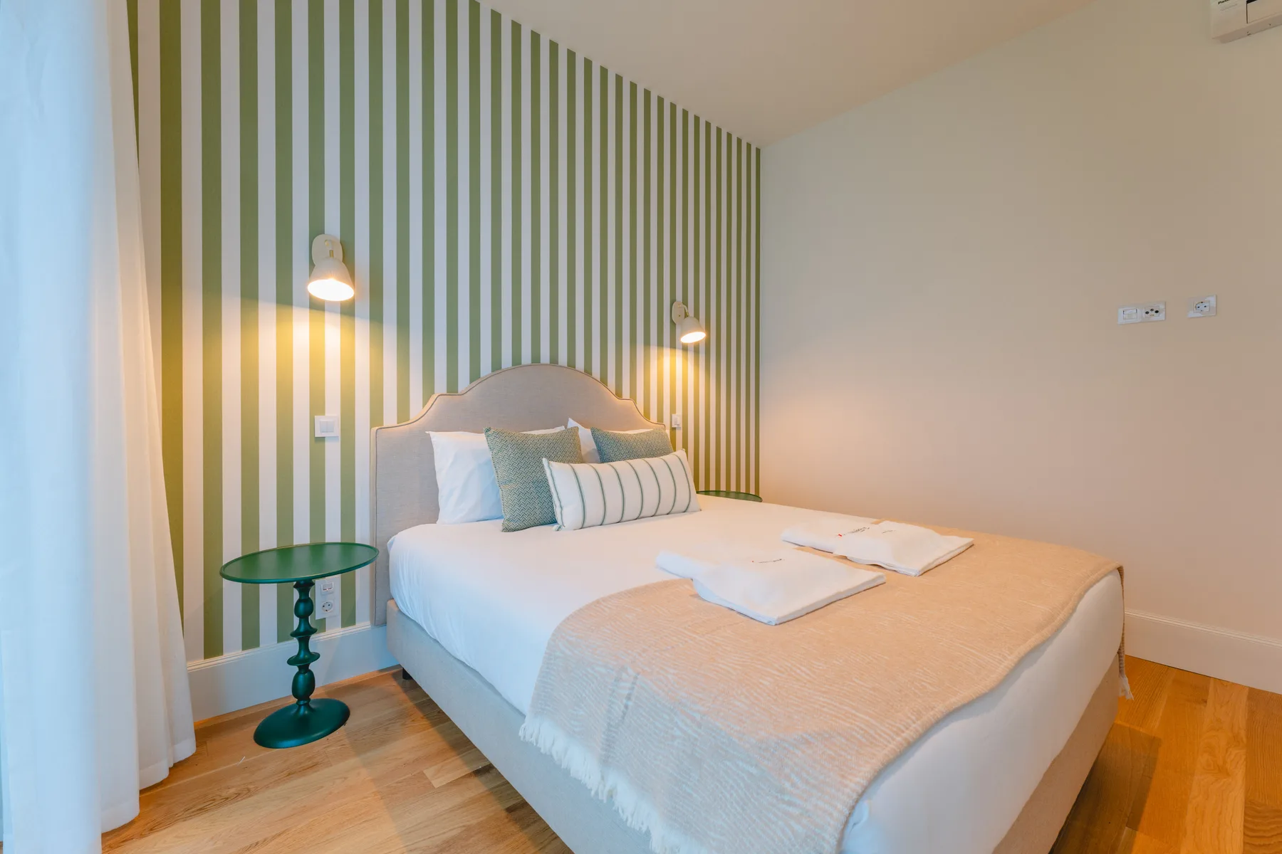 Un dormitorio con una cama, una pared decorativa a rayas y una pequeña mesa auxiliar.