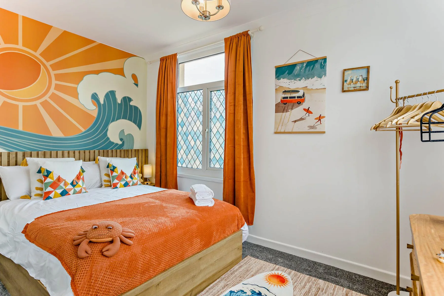 A bedroom with an orange-covered bed and a colorful sun-and-wave mural.