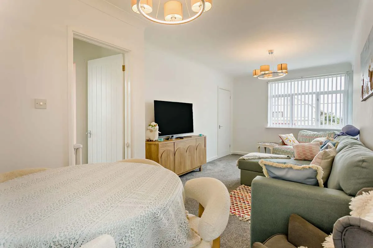 Un dormitorio y sala de estar luminosos con cama, televisor y asientos.