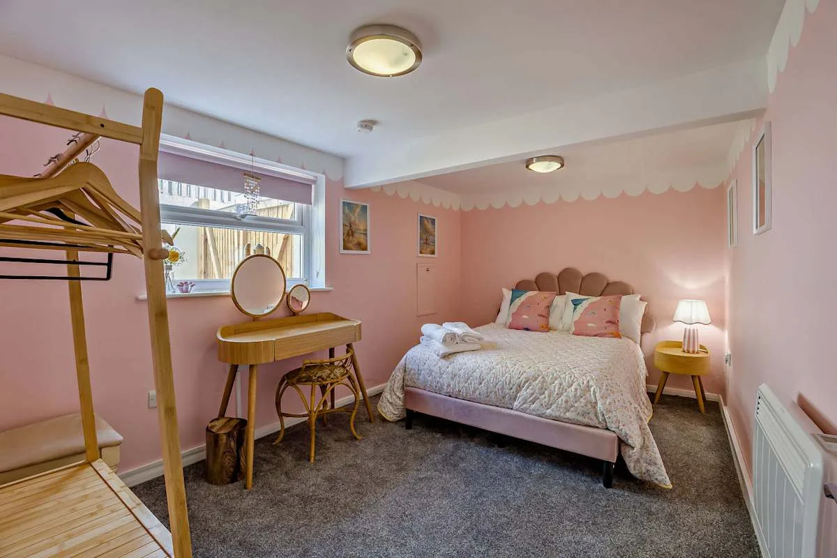 Un dormitorio rosa con una cama, un tocador y un perchero independiente.