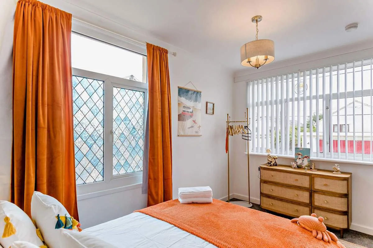 Un dormitorio luminoso con cortinas naranjas, una cama y una cómoda de madera.