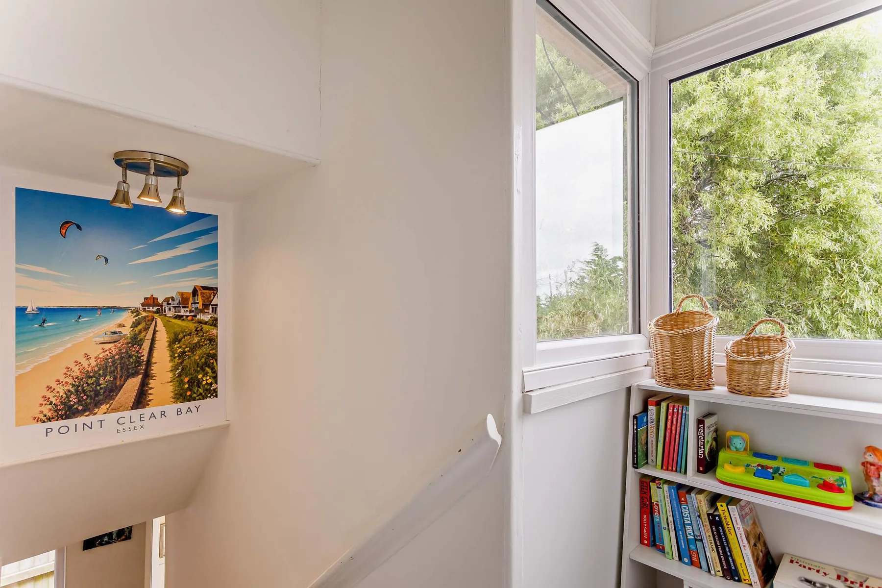 Un rincón luminoso junto a la ventana, con libros y cestas en estantes y un póster de playa.