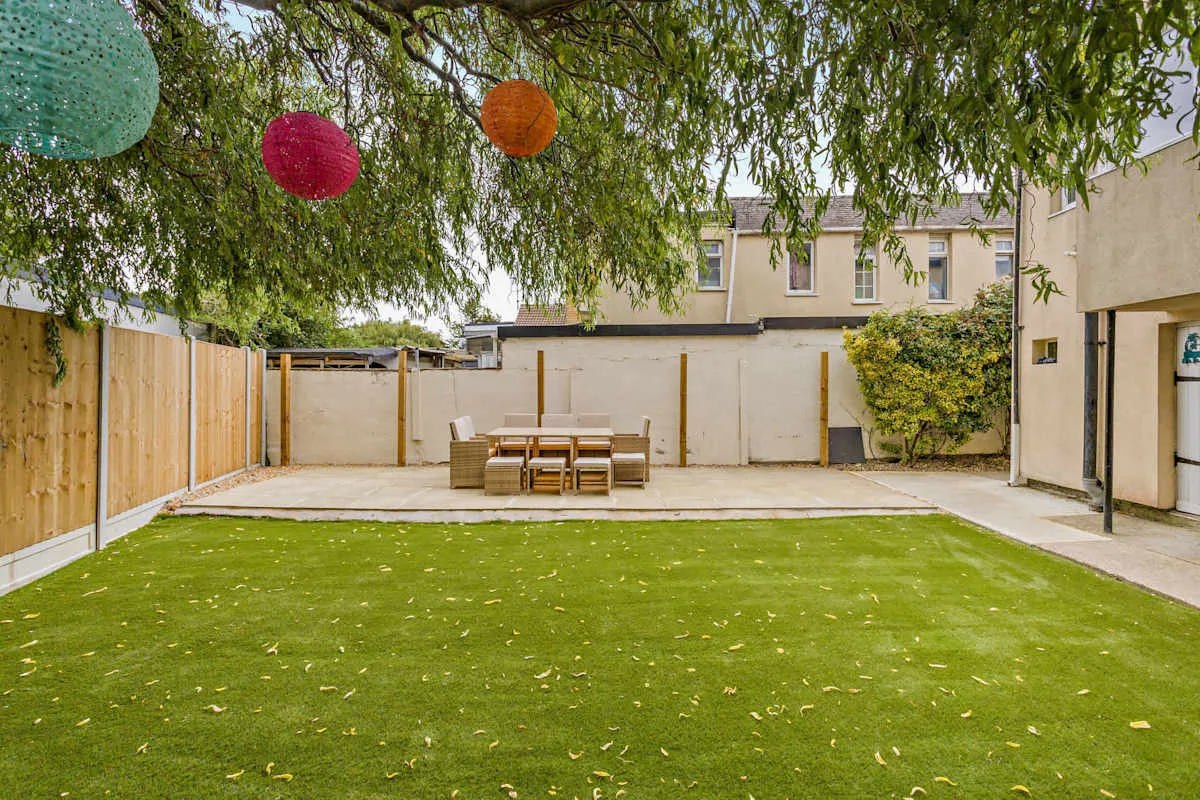 Un patio con césped verde, asientos al aire libre y adornos colgantes de colores.