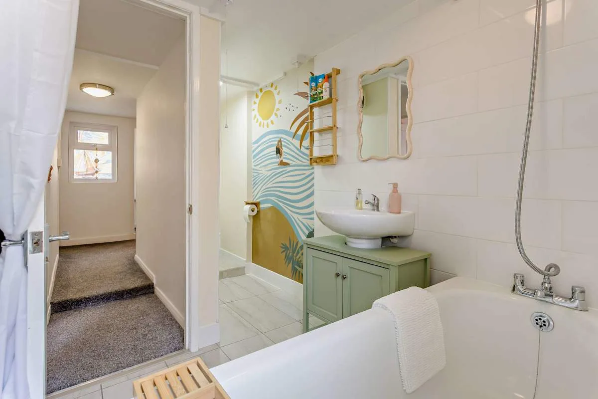 Baño con bañera, lavabo y un colorido mural de temática oceánica.