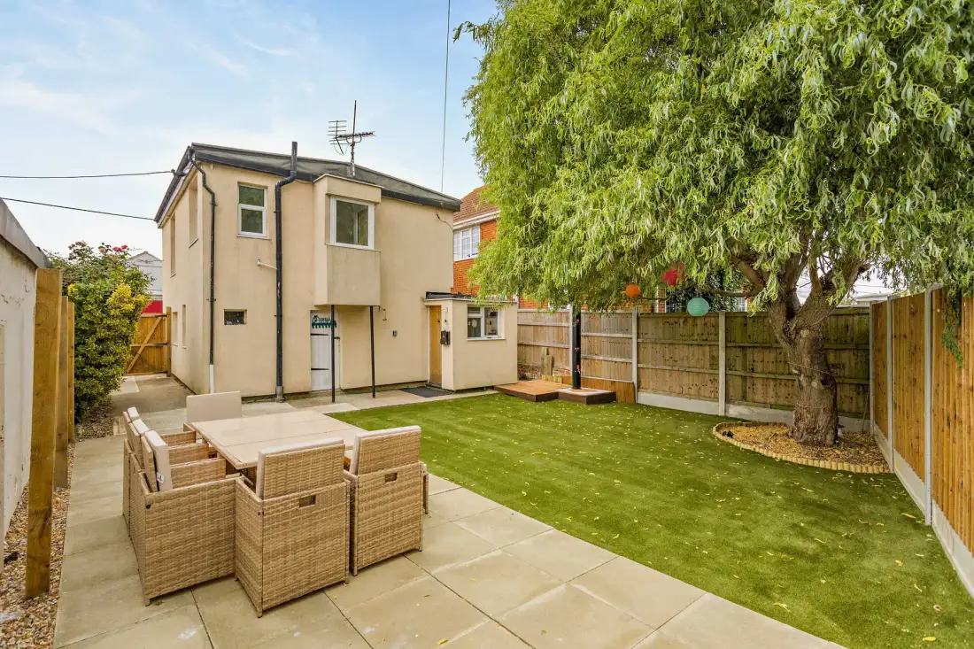 A backyard patio with outdoor seating, a lawn, and a large tree.