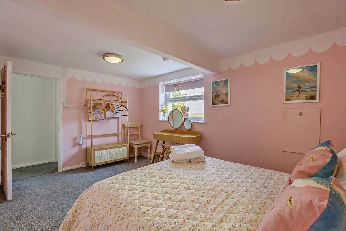 Un dormitorio rosa con una cama, una ventana y un pequeño tocador.