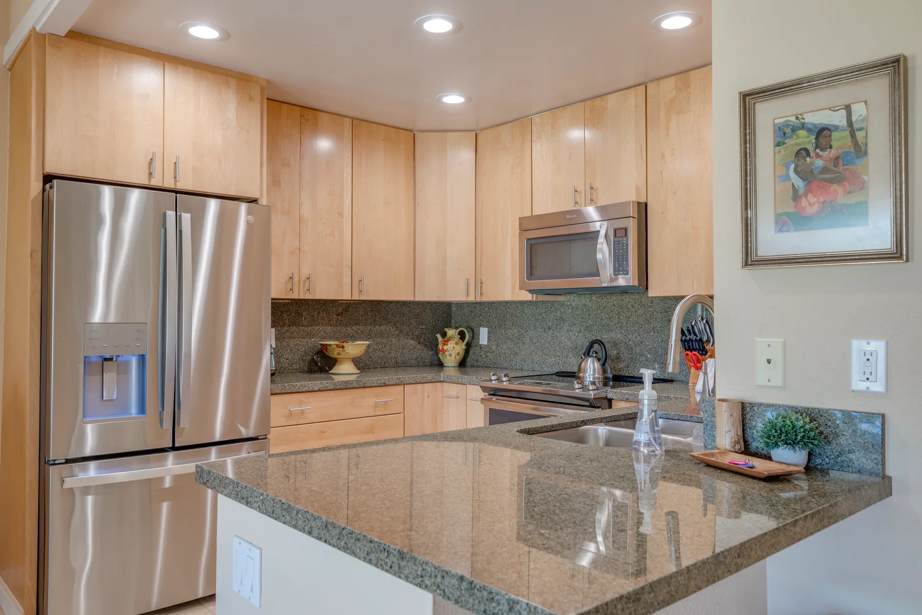 Una cocina con gabinetes de madera clara y una gran isla con encimera de piedra.