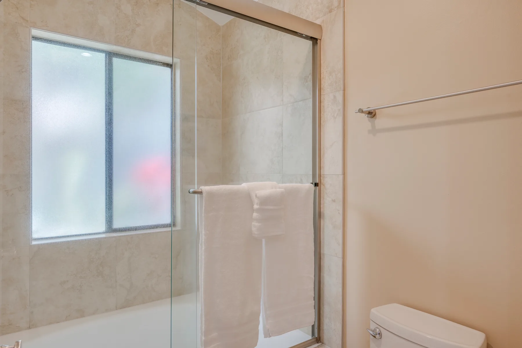 Un baño con ducha de vidrio, ventana y toallas colgadas cerca.