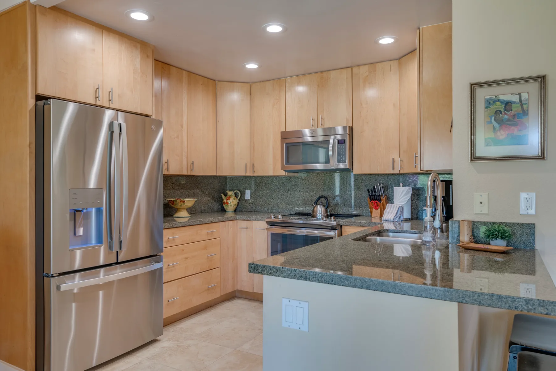 Una cocina con gabinetes de madera clara, electrodomésticos de acero inoxidable e isla central.