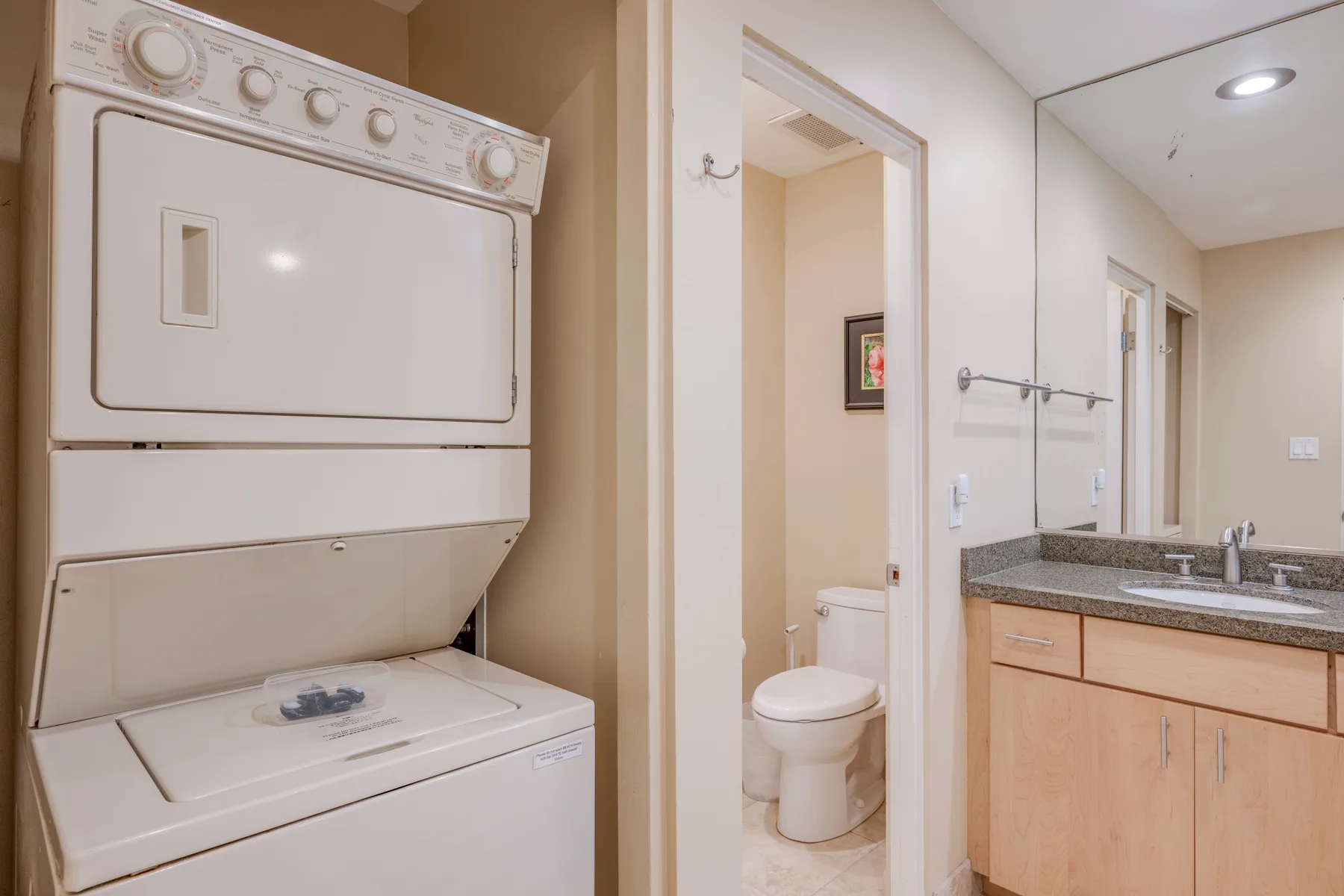 Zona de lavandería con lavadora y secadora apiladas junto al lavabo del baño.