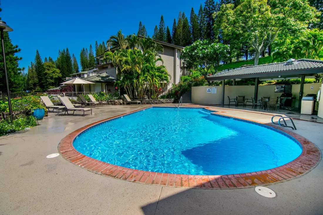 Una piscina al aire libre junto a una terraza pavimentada y una zona de asientos con sombra.