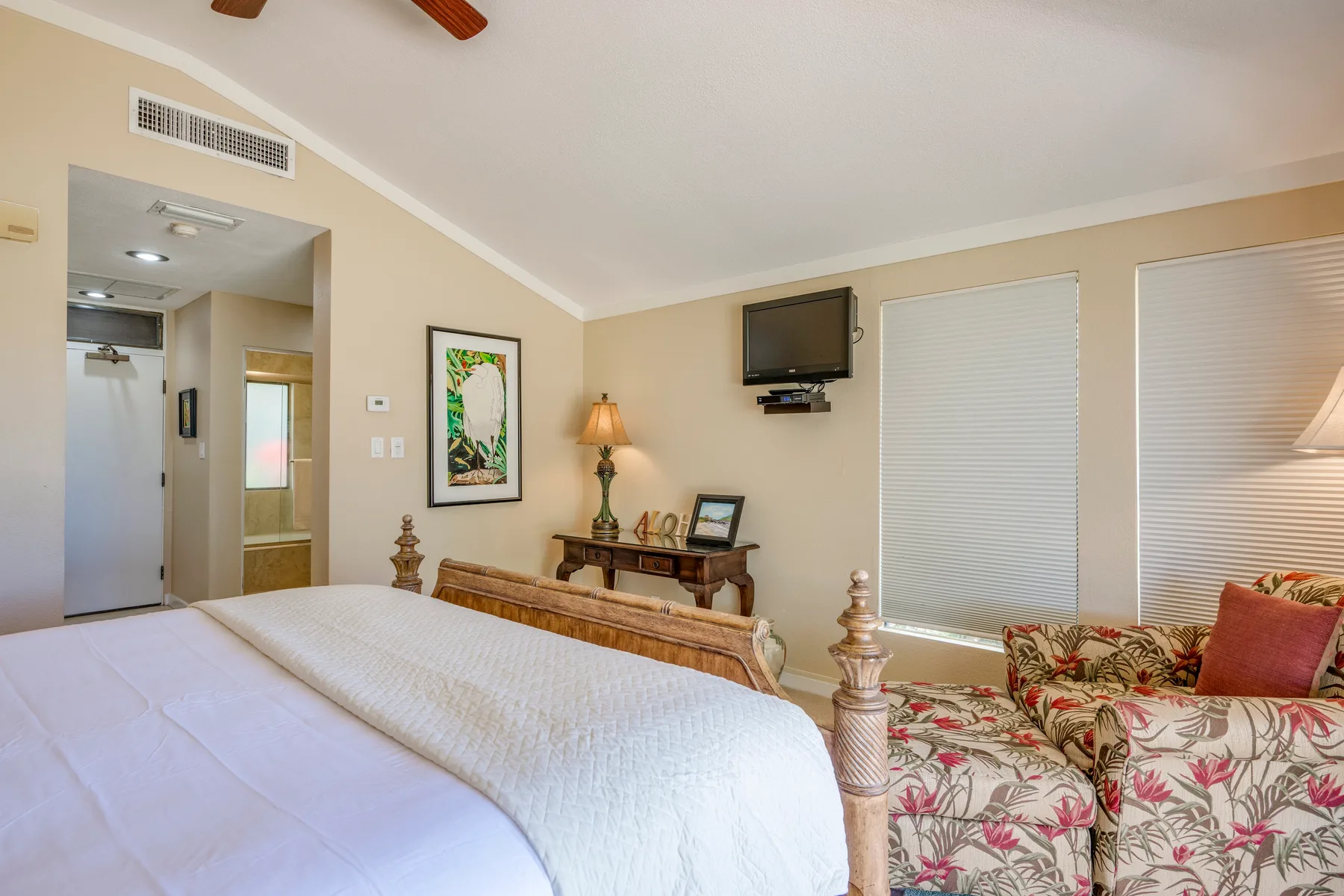 Un dormitorio con una cama, una zona de estar floral y ventanas con persianas cerradas.