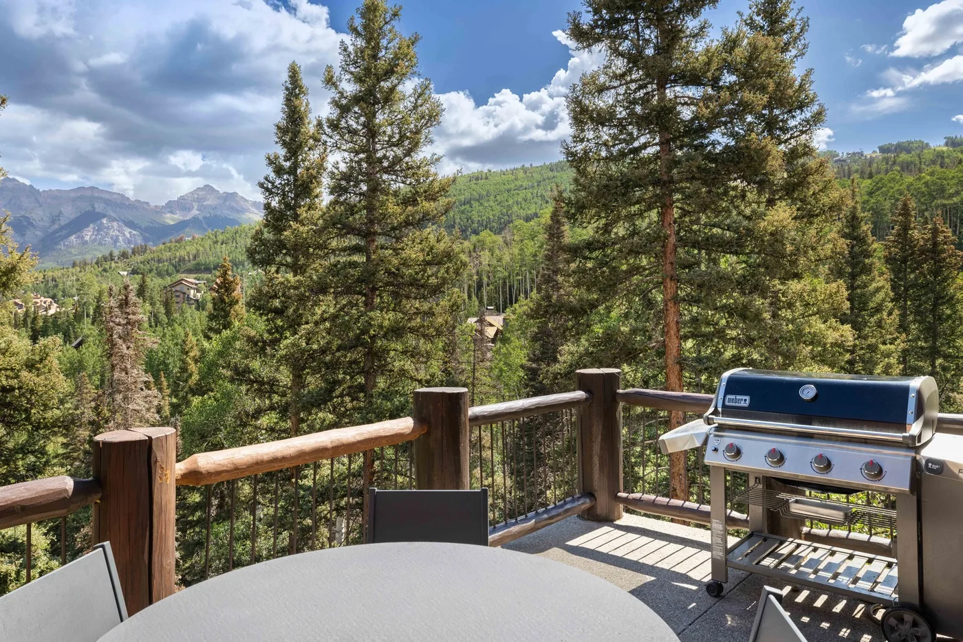 A patio overlooks a forested mountain landscape, with a grill beside the railing.