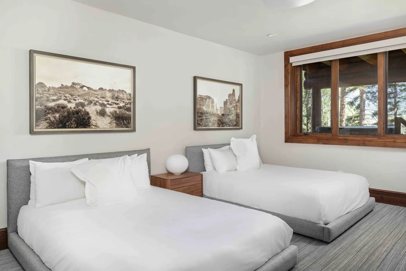 A bedroom with two beds, framed pictures, and a large wooden-framed window.