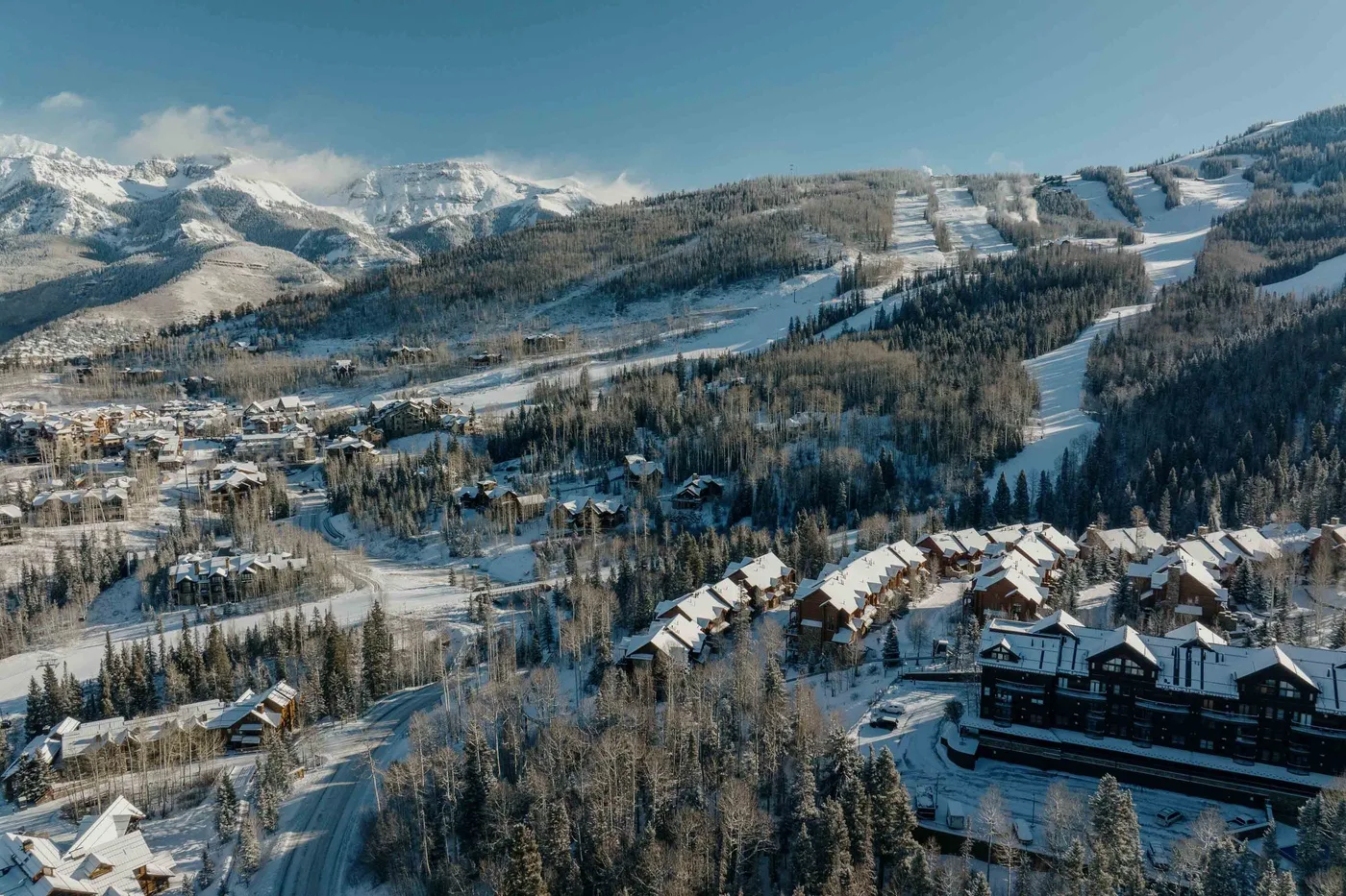 Aerial view of a snowy mountain resort with wooded slopes and buildings.
