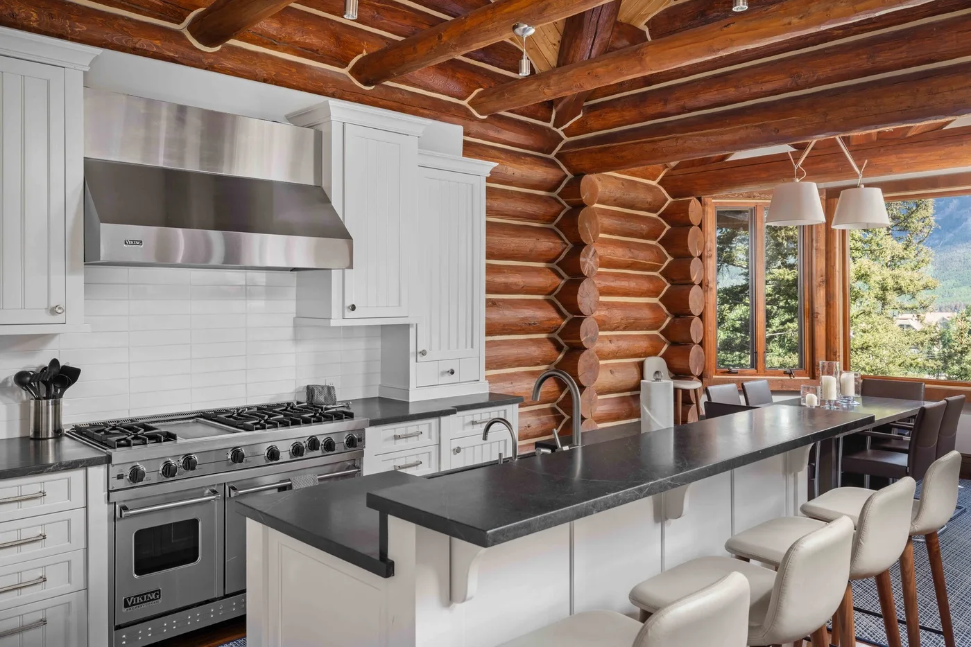 A kitchen with a long island and a row of seating beneath exposed wooden beams.