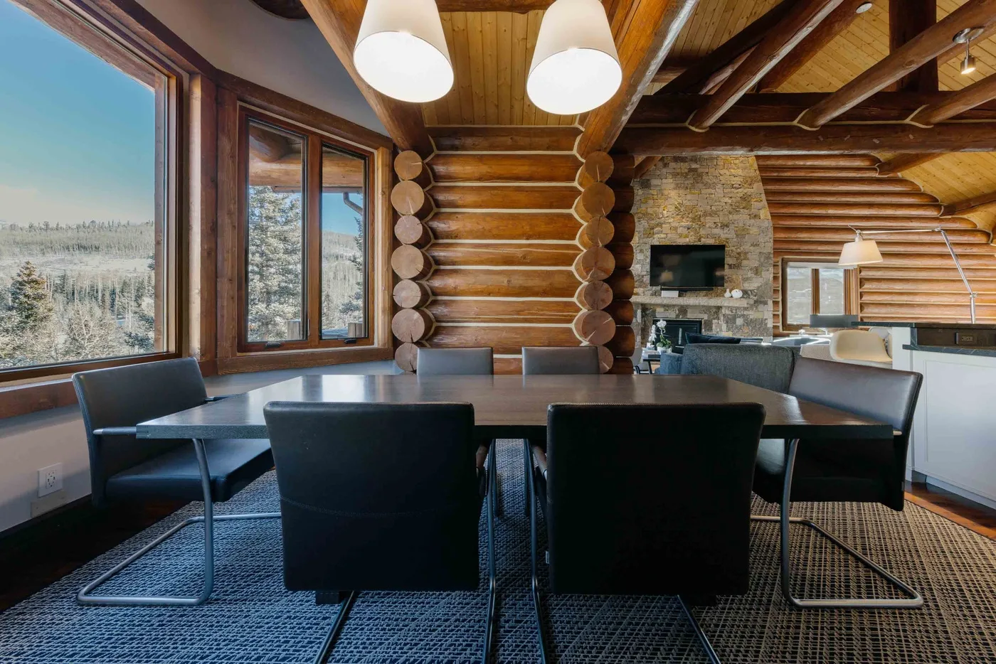 A dining area with a table and seating beside large windows in a log cabin.