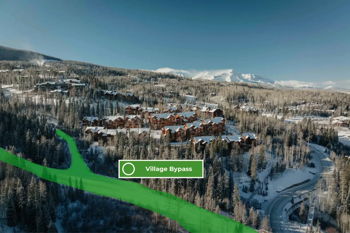Snow-covered mountain village surrounded by forest, with a marked route crossing the foreground.