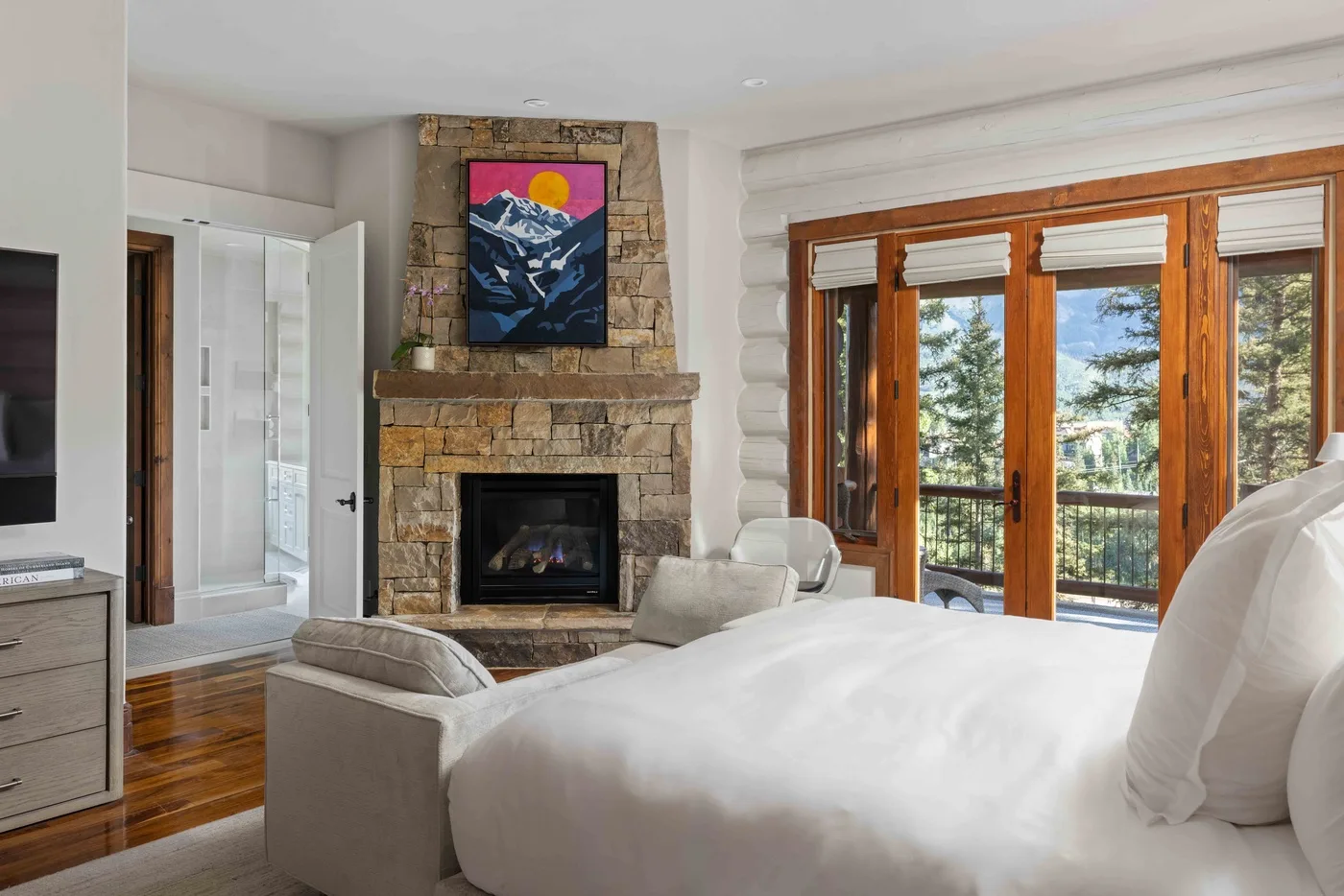 A bright bedroom with a bed, stone fireplace, and wooden-framed windows.