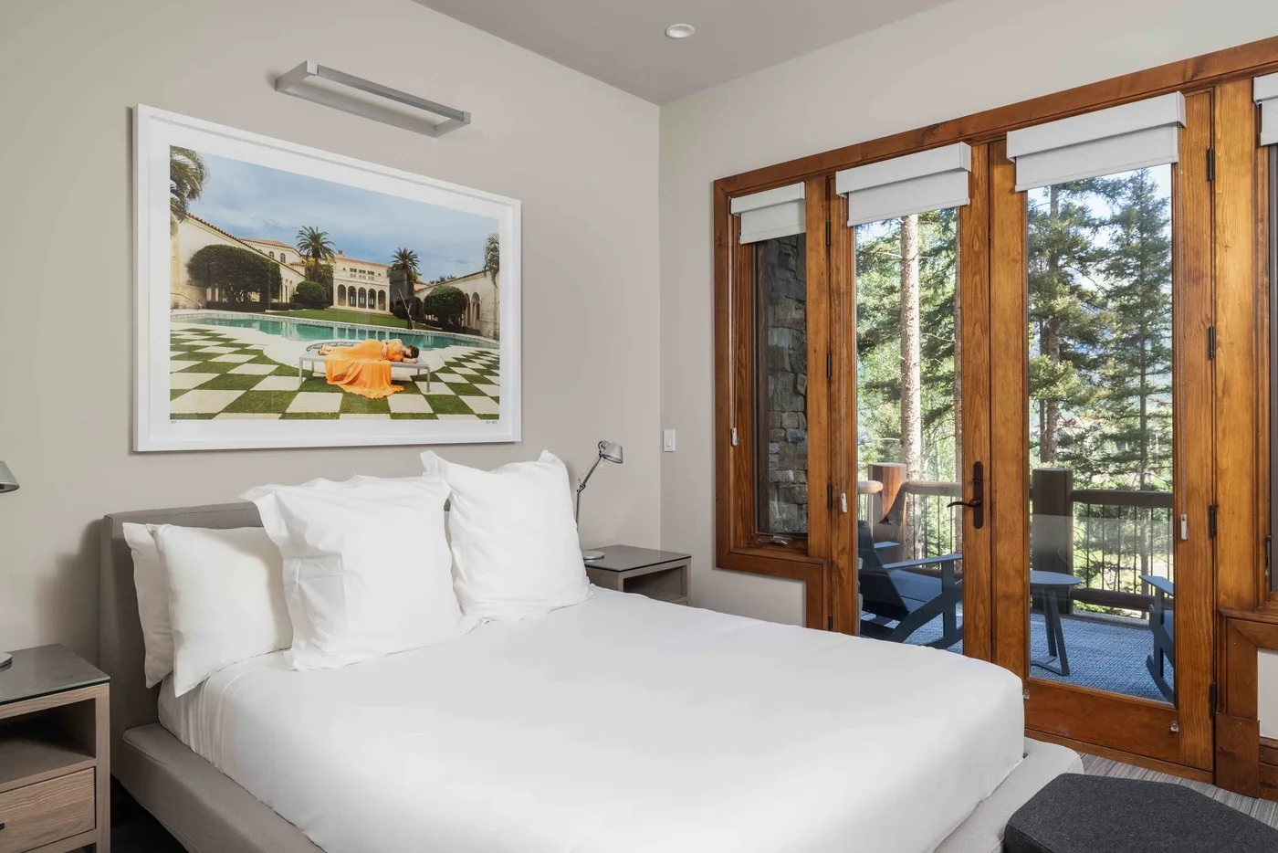 A bright bedroom with a neatly made bed beside wood-framed glass doors.
