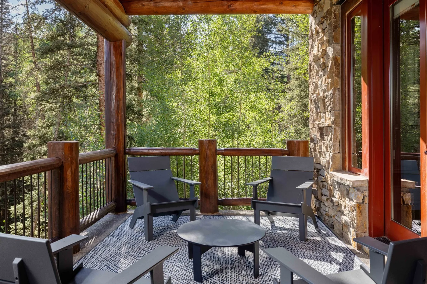 A covered outdoor deck with seating and a view of surrounding trees.