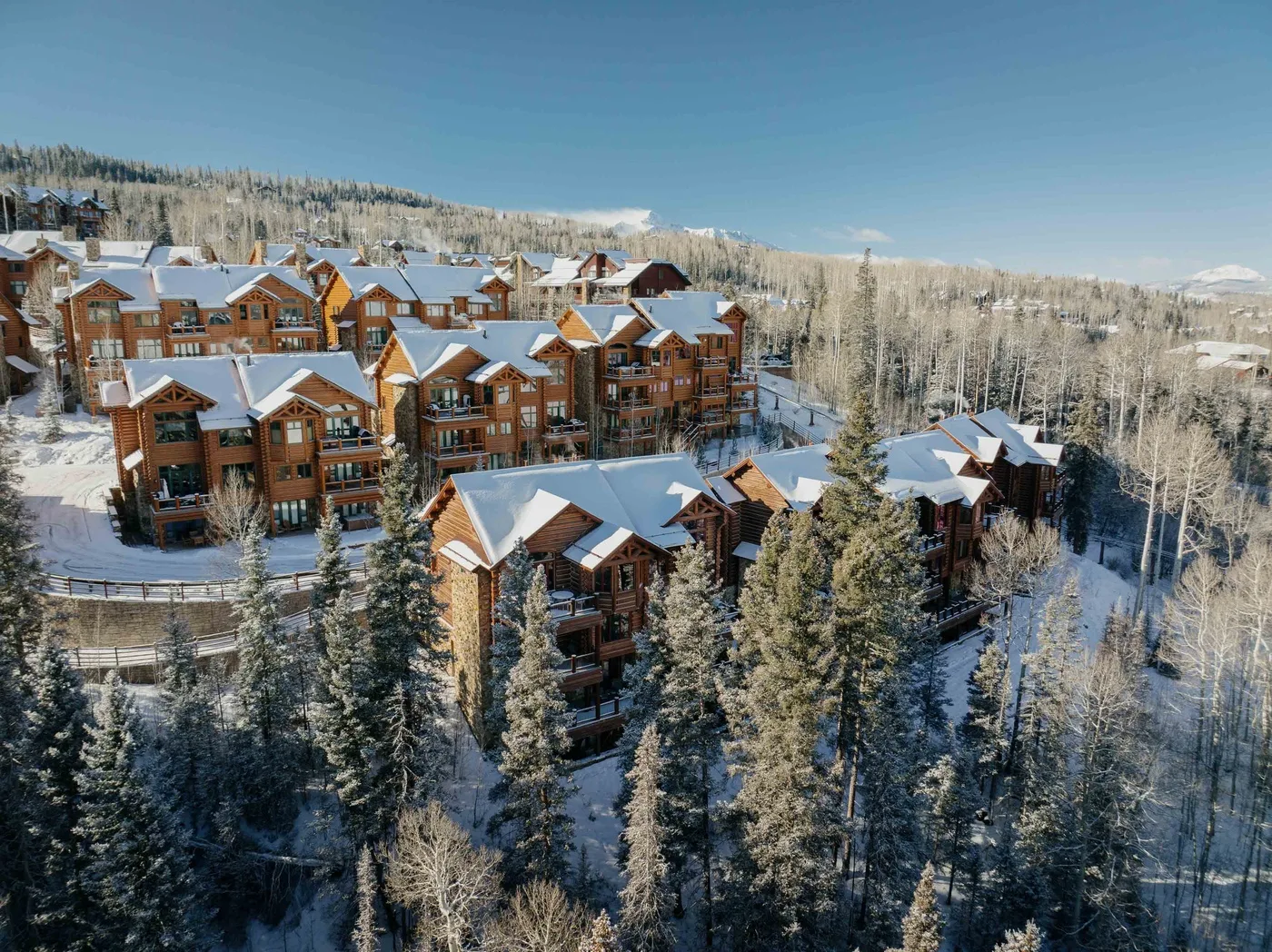 Snow-covered lodge buildings sit among evergreen trees on a wooded hillside.