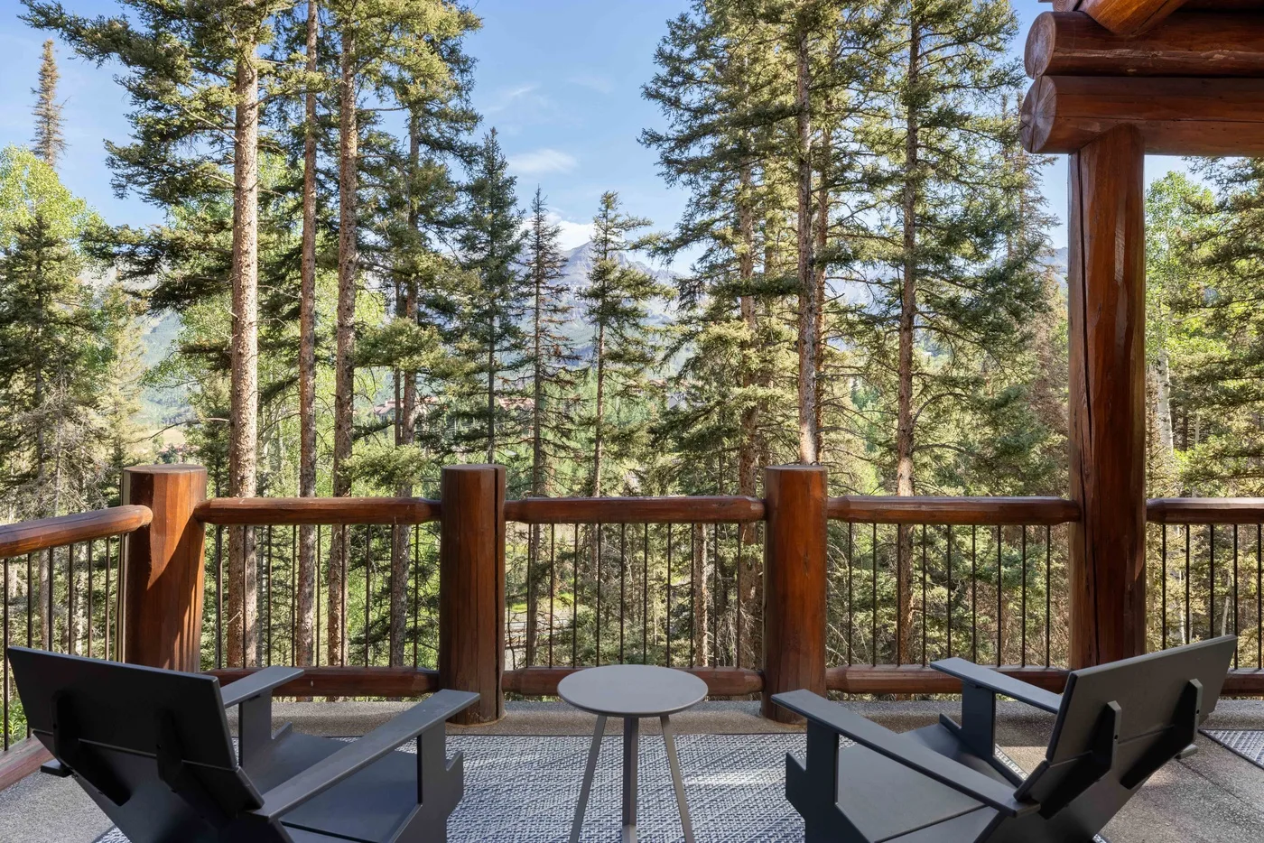 An outdoor deck with seating overlooks a forest of tall trees.