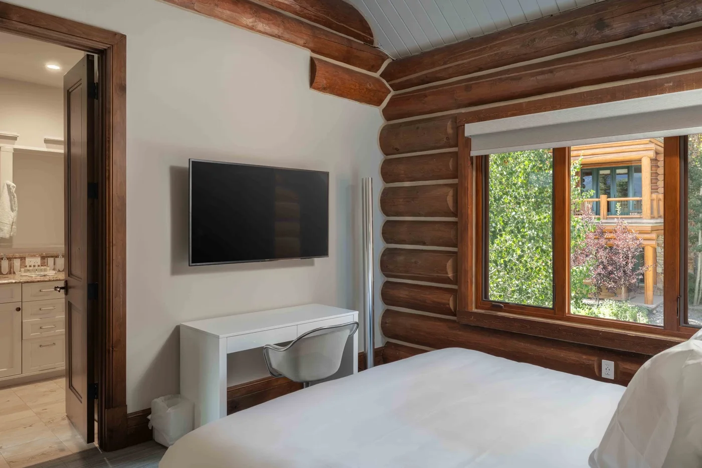 A bedroom with a bed, a wall-mounted television, and a large window.