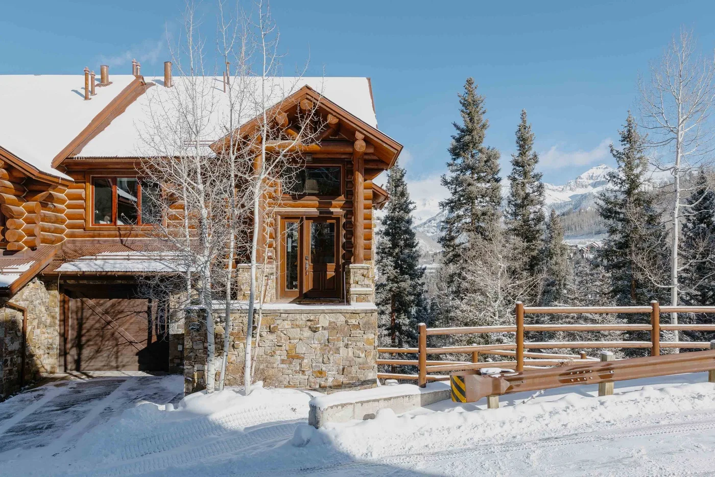 A log cabin stands beside a wooden railing in a snowy mountain landscape.