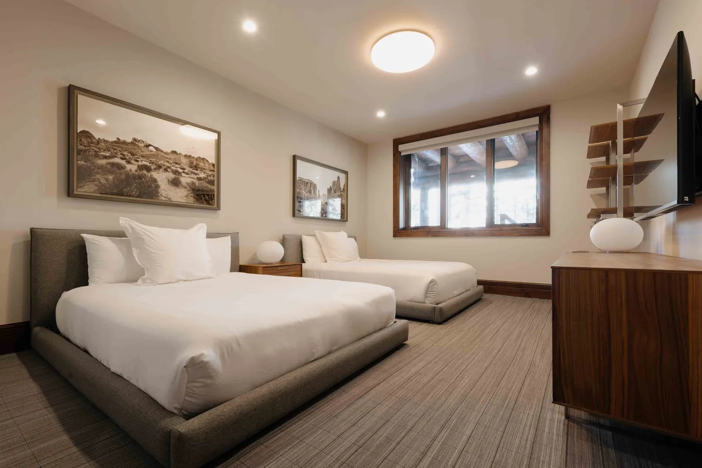 A bedroom with two beds, framed artwork, and a large window.
