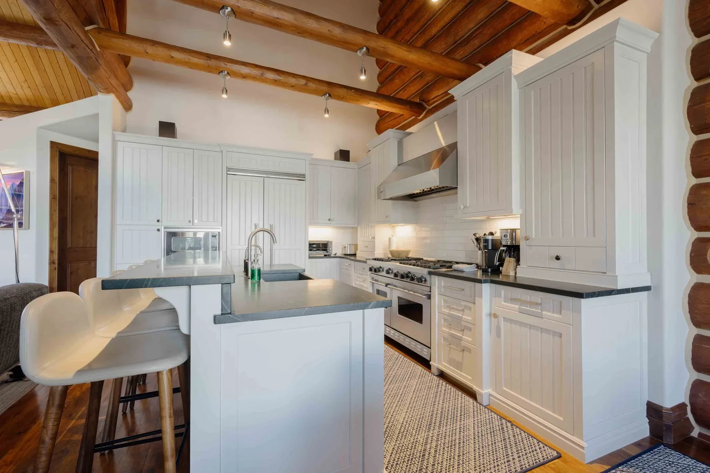 A bright kitchen with white cabinetry, a central island, and exposed wooden ceiling beams.