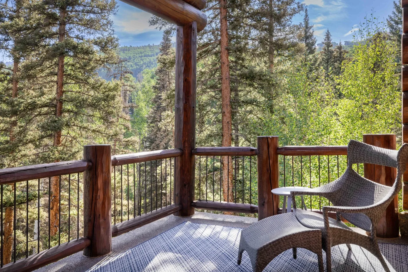 A covered wooden deck overlooks a forested mountain landscape.