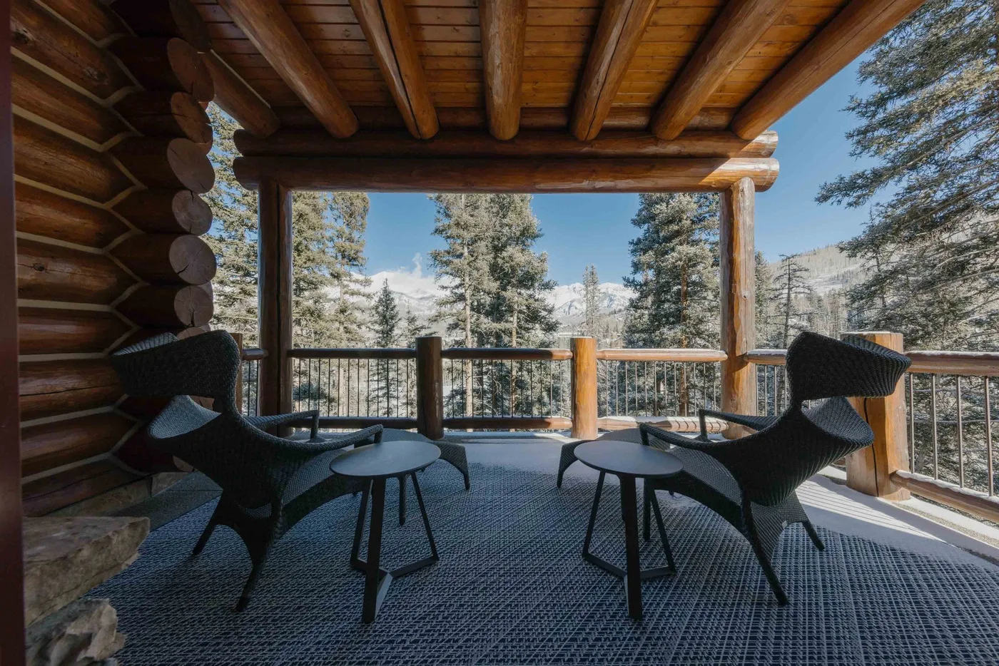 A covered wooden deck with seating and tables overlooks a tree-filled mountain landscape.