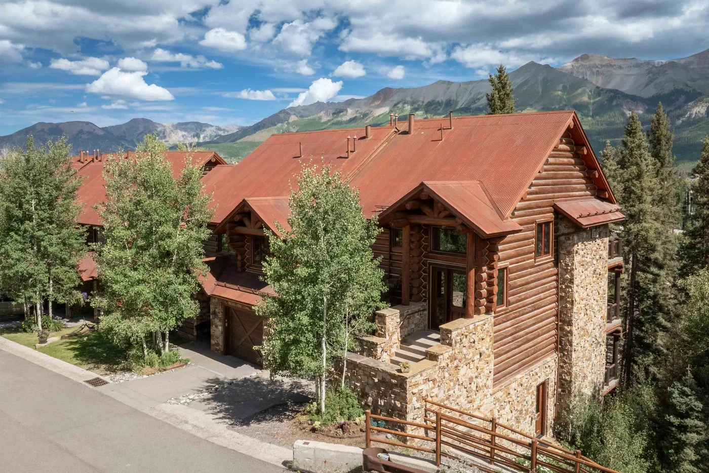 A log cabin building with red roofs stands among trees beneath a mountain range.