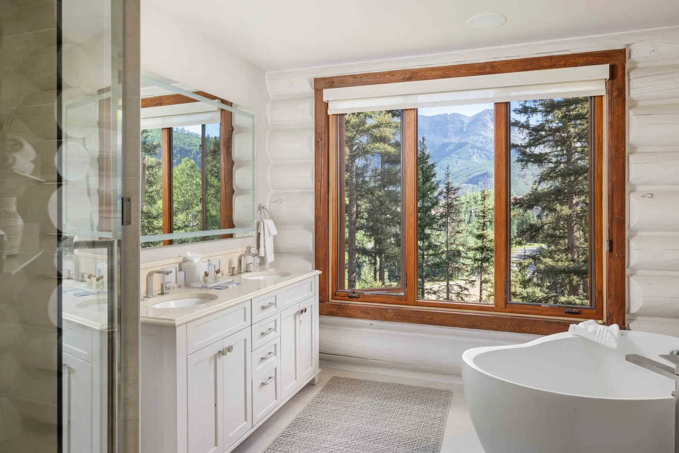 A bright bathroom with a white vanity and a large window overlooking trees and mountains.