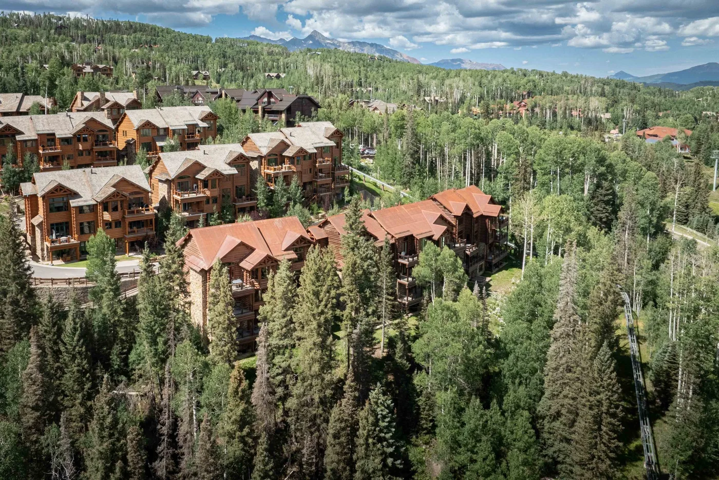 A cluster of chalet-style buildings sits among dense trees in a mountain landscape.