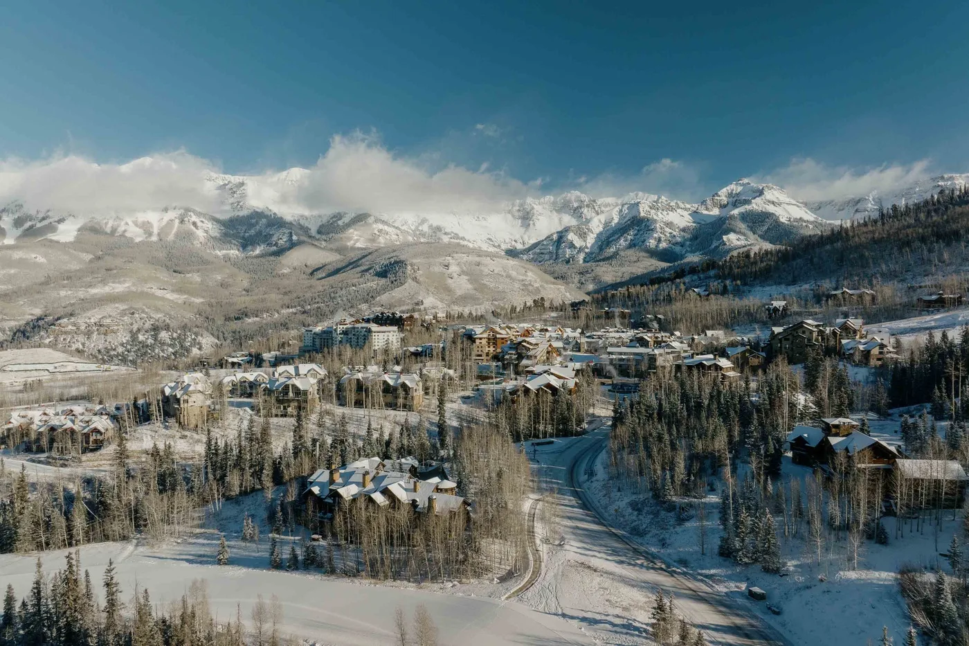 A snow-covered mountain resort with buildings and a winding road beneath the peaks.