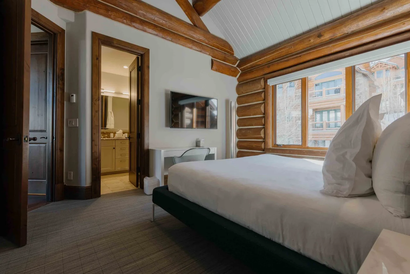 A bedroom with a large bed beside a window and wooden ceiling beams.